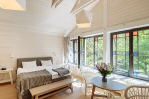 Un dormitorio con cama, mesita de noche y vistas a la vegetación a través de amplias ventanas.