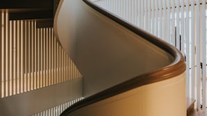 A curved staircase with wooden steps and a white handrail, leading to a room with vertical blinds. - Villa Santa Hotel (Cesis)