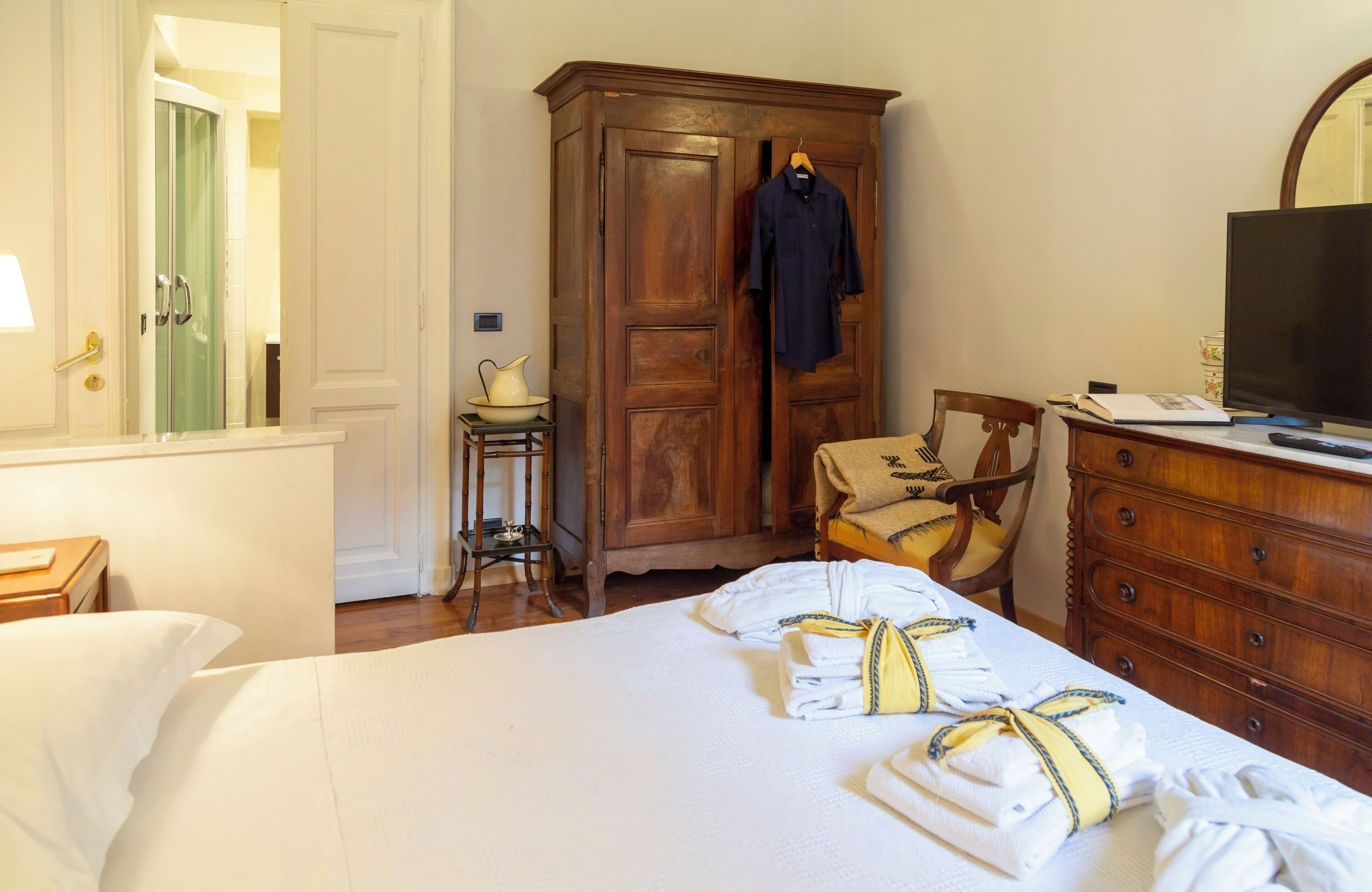 A hotel room with a bed, a wooden wardrobe, a chair, a desk with a television, and a mirror.