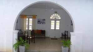 A room with a white wall, an arched doorway, a sofa, a dining table with chairs, and two potted plants. - Sarvodaya Samma Vaasa Resedence (Kandy)
