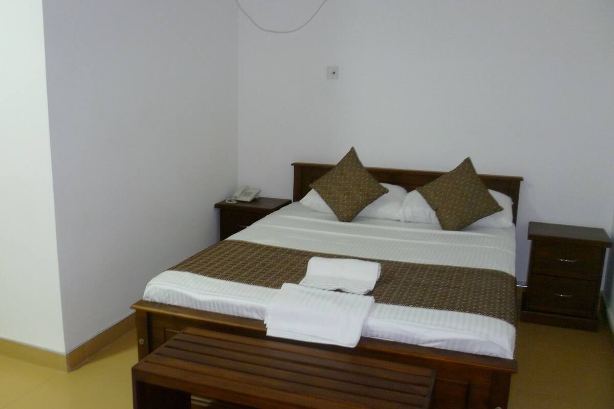 A neatly made bed with a brown headboard, a bedside table with a phone, and a small bedside table with a lamp.