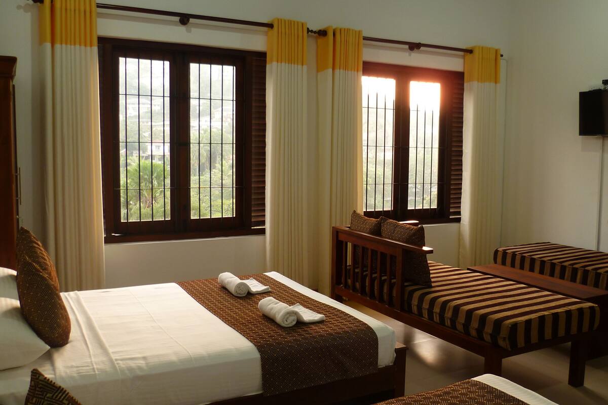 A hotel room with two beds, a TV, and large windows with curtains.