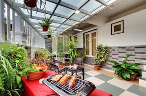 A covered patio with a grill, seating, and potted plants.