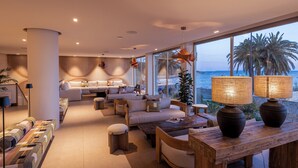A modern living room with a sofa set, wooden coffee table, and large windows overlooking the sea. - Hotel Simbad (Ibiza Town)