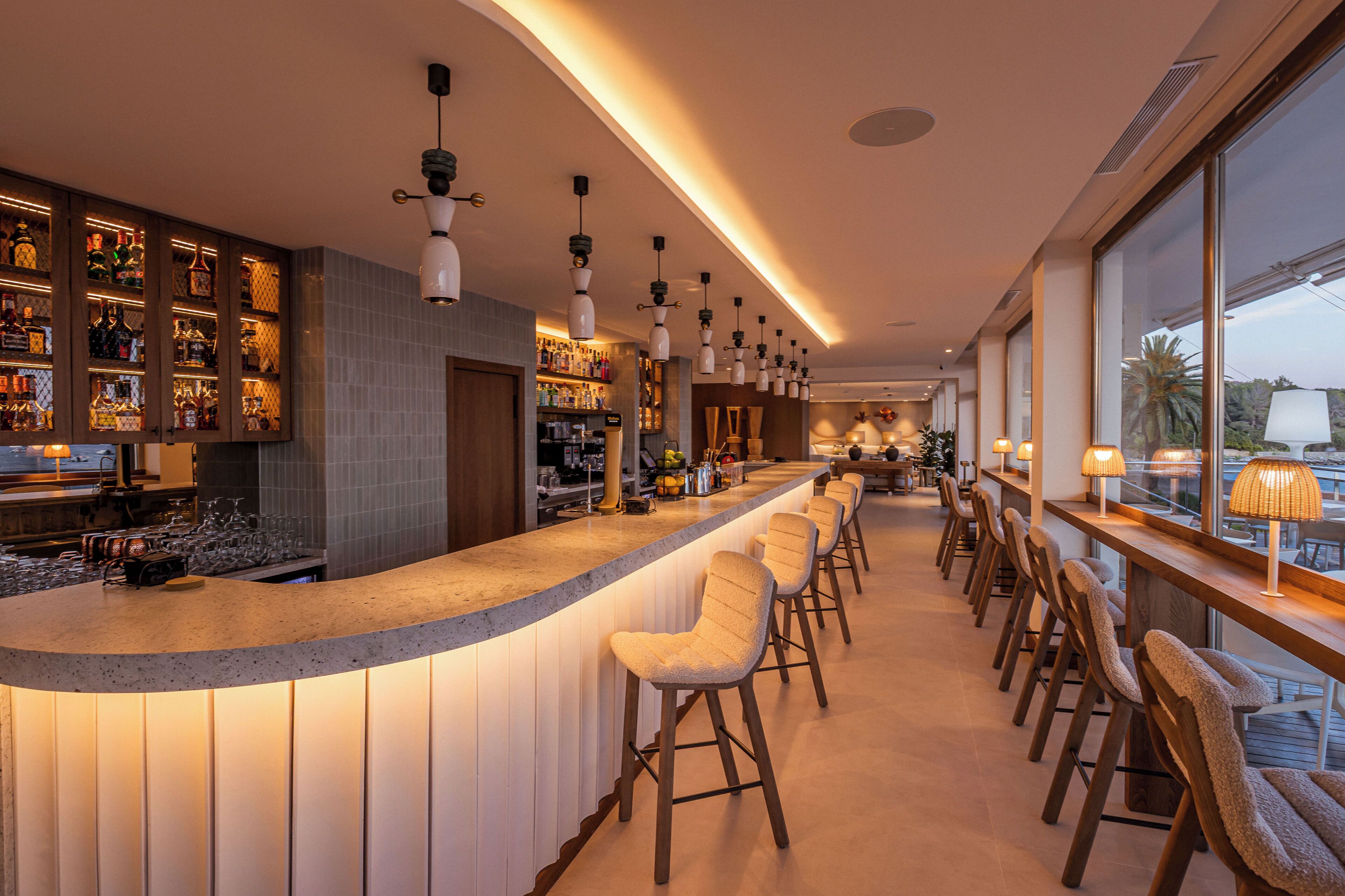 A bar with a curved counter, multiple stools, and hanging pendant lights.