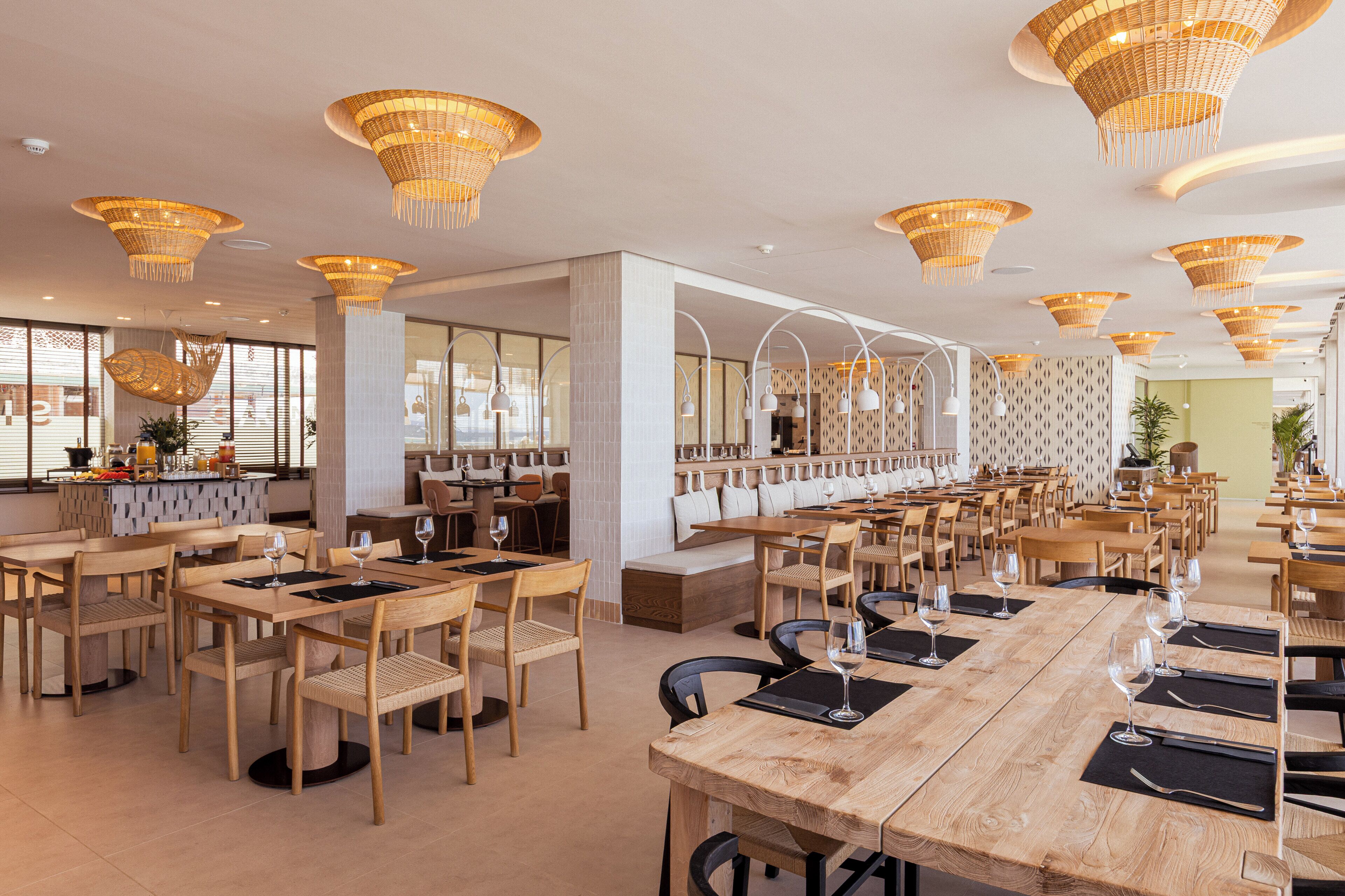 A spacious restaurant with wooden tables and chairs, large hanging wicker chandeliers, and a long counter with seating.