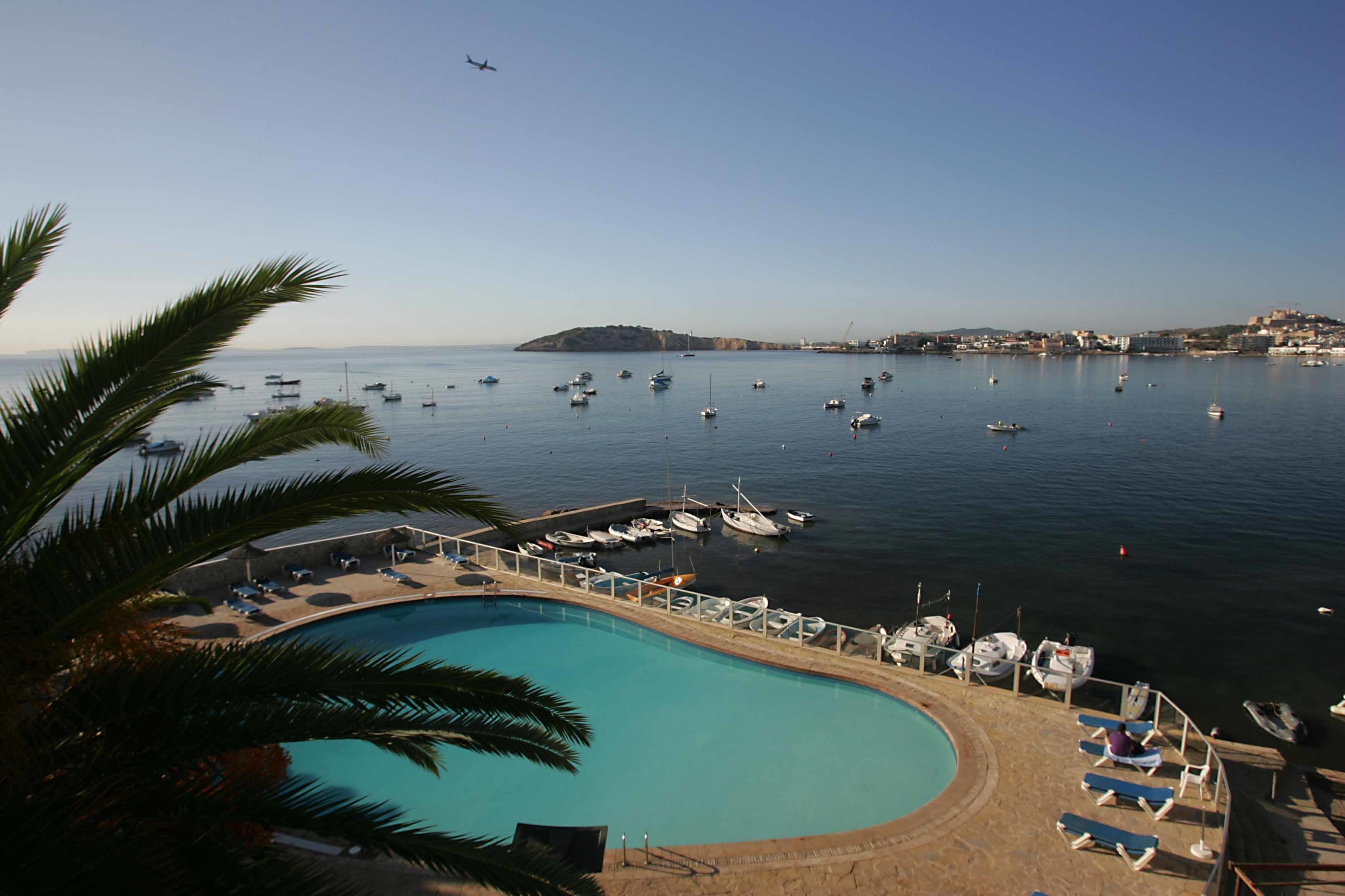 Vista de la piscina con barcos, cielo despejado y una isla distante.