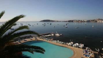 Vista de la piscina con barcos, cielo despejado y una isla distante.