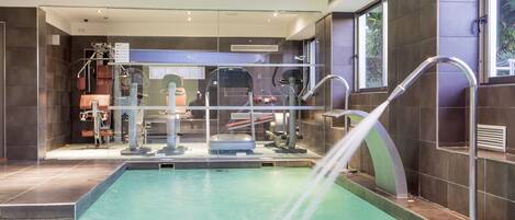 A modern indoor pool area with a water feature, exercise equipment, and a view of the outside.