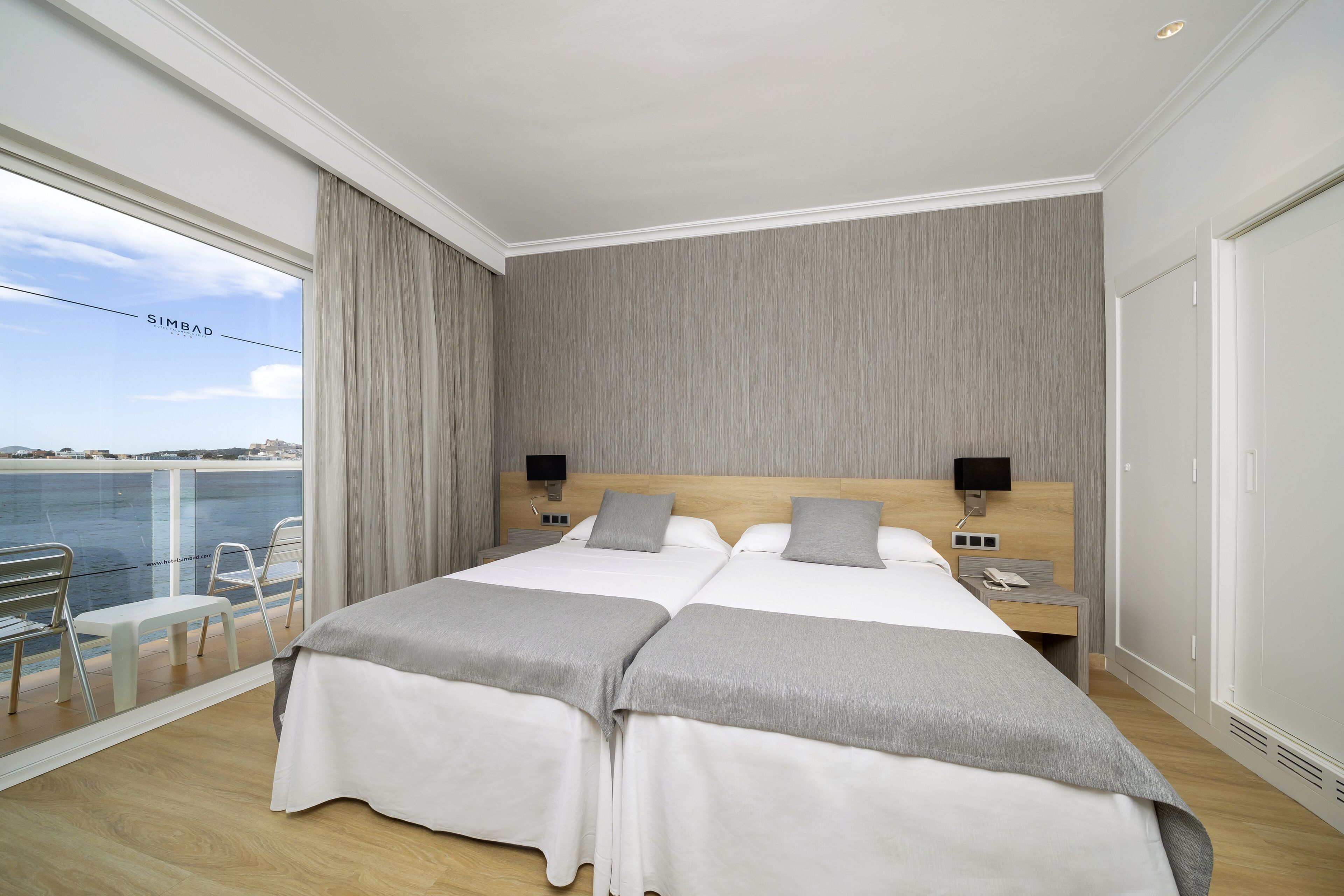 Une chambre d’hôtel avec deux lits, un balcon donnant sur la mer, un bureau avec une chaise et une armoire.