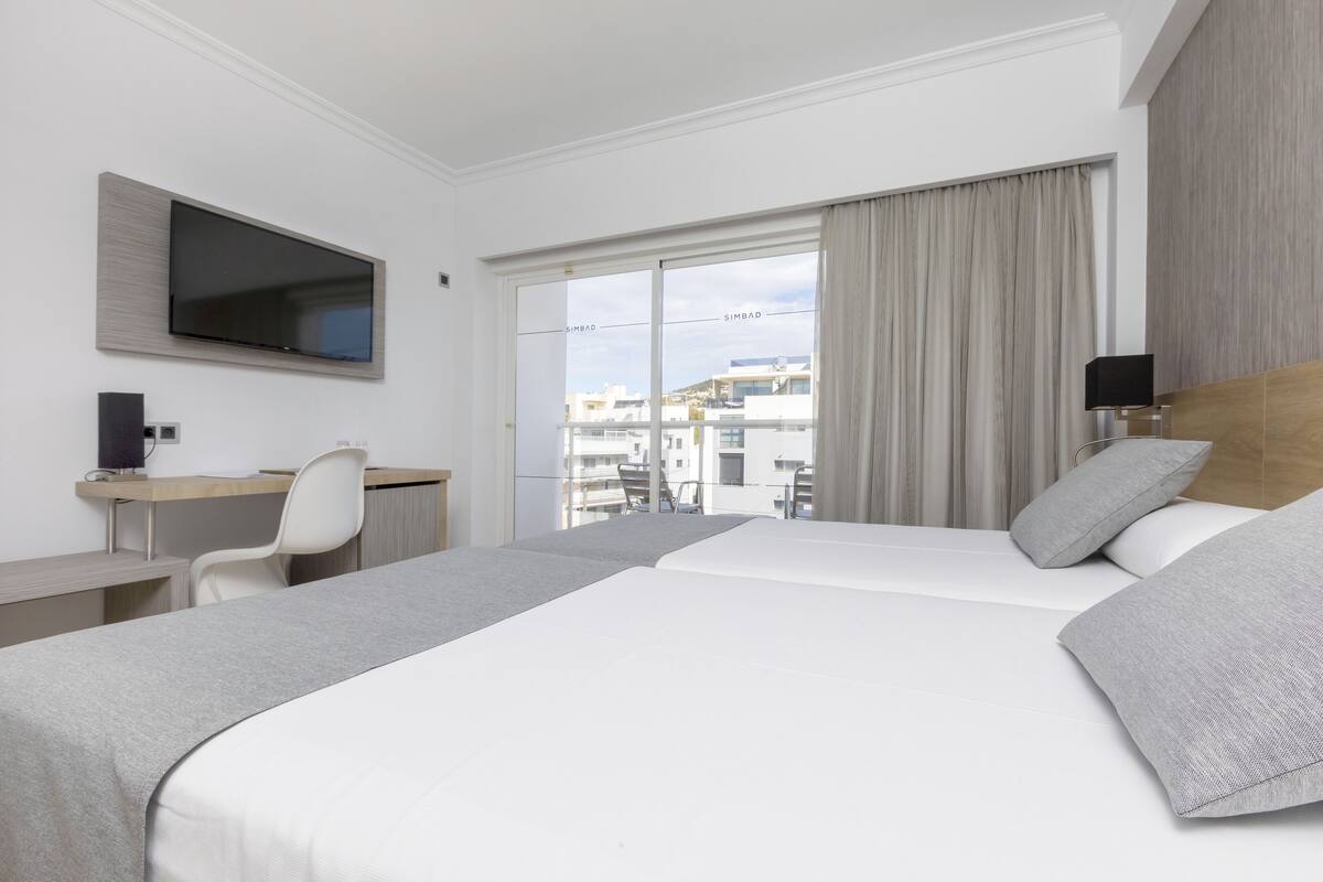 Habitación de hotel con una cama grande, un escritorio, una silla, un televisor montado en la pared y vistas a la ciudad por la ventana.