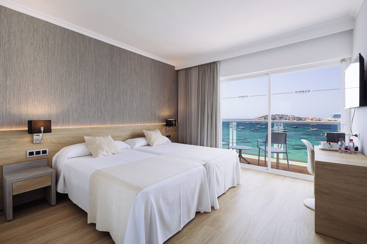 Habitación de hotel con una cama grande, un escritorio, una silla, una mesita de noche y vista al mar.