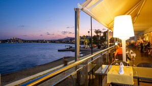A seaside restaurant with outdoor seating overlooking the water, featuring a large table and a bright lamp. - Hotel Simbad (Ibiza Town)