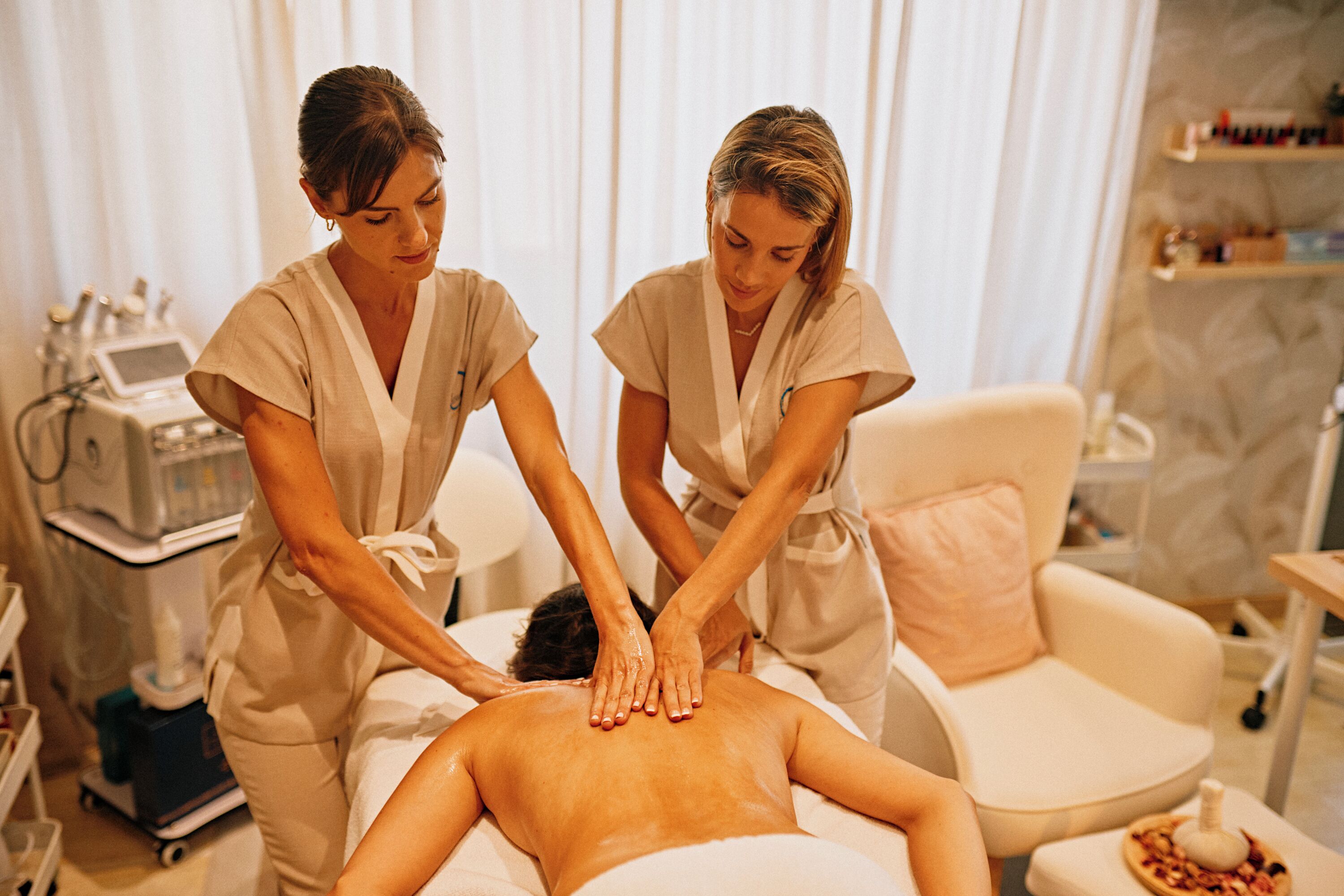A massage therapy room with a client receiving a back massage. Two therapists are attending to the client.
