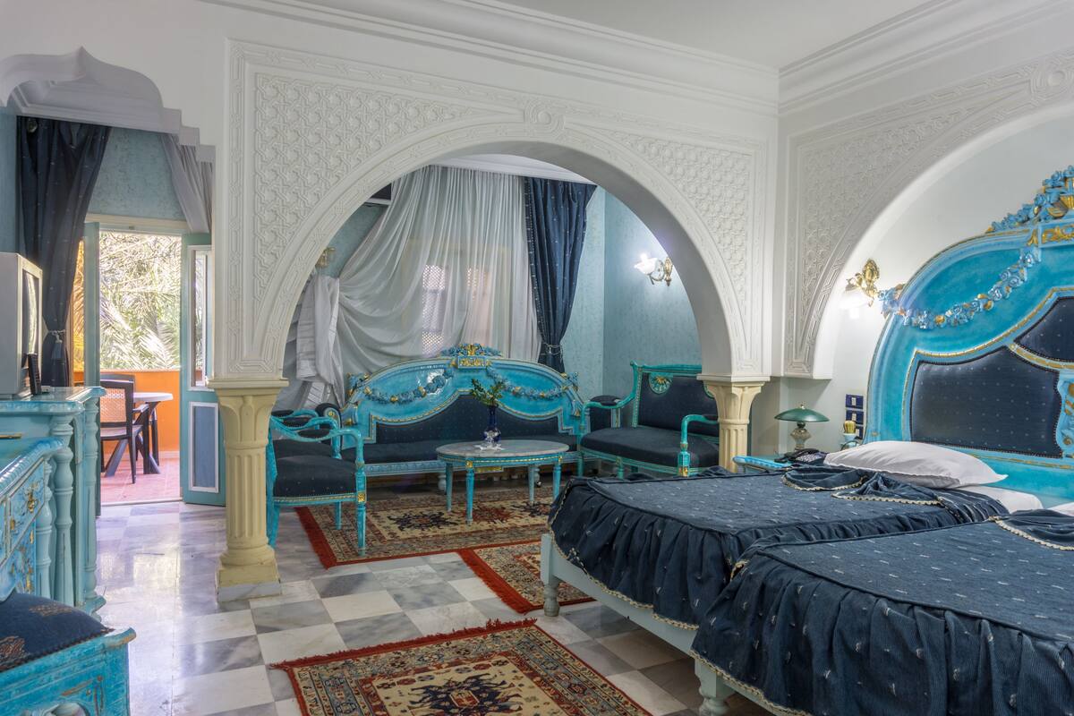 A room with two beds, a sofa, a table, and a decorative archway.