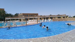 A swimming pool with lounge chairs and a building with arched windows in the background. - Hotel Jugurtha Palace (Gafsa)
