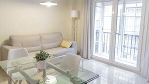 A modern living room with a glass dining table, a sofa, and a potted plant. - Apartamento Ulises Suite 1 (Málaga)