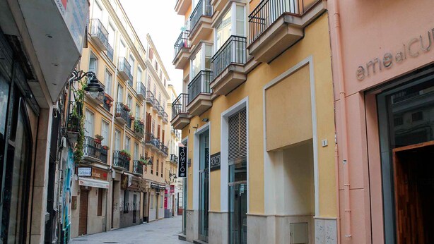 A narrow street lined with multi-story buildings, some with balconies and potted plants. - Apartamento Ulises Suite 1 (Málaga)