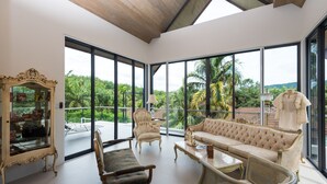 Una habitación amplia con ventanas grandes, un sofá cómodo, una mesa de centro de madera y un sillón clásico.