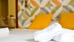 A neatly made bed with white linens and rolled towels, a yellow pillow, and a geometric patterned wall in the background. - Apartamento Ulises Suite 2 (Málaga)