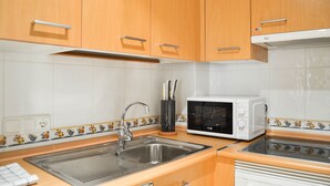 A kitchen with wooden cabinets, a microwave, a sink, and a tiled backsplash. - Apartamento Ulises Suite 2 (Málaga)