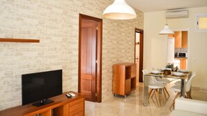 A modern living room with a flat-screen TV, wooden furniture, a dining area with a glass table, and pendant lighting. - Apartamento Ulises Suite 2 (Málaga)