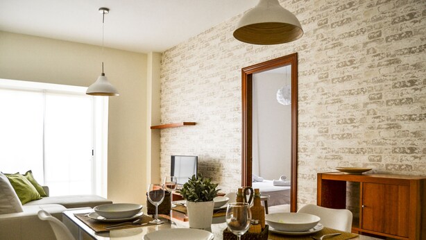 A dining area with a glass table, chairs, and a brick-patterned wall. - Apartamento Ulises Suite 2 (Málaga)