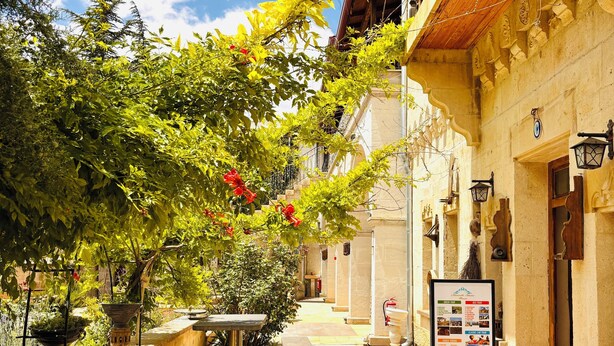 A narrow alleyway with a stone bench, potted plants, and a signboard. - Mozaik Otel (Avanos)