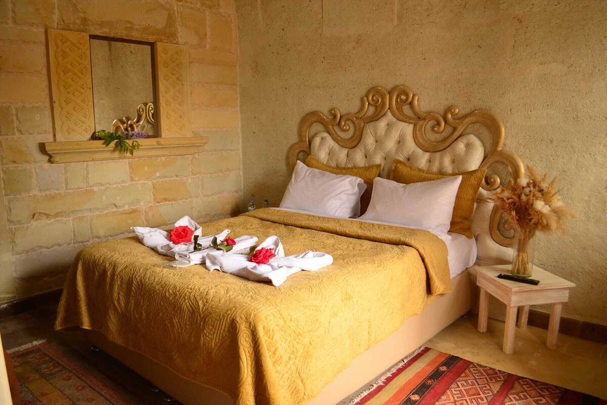 Una cama con colcha dorada, almohadas blancas y un cabecero decorativo.