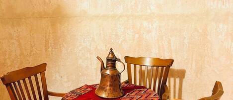 A dining table with a metal pitcher, a red patterned tablecloth, and four wooden chairs.