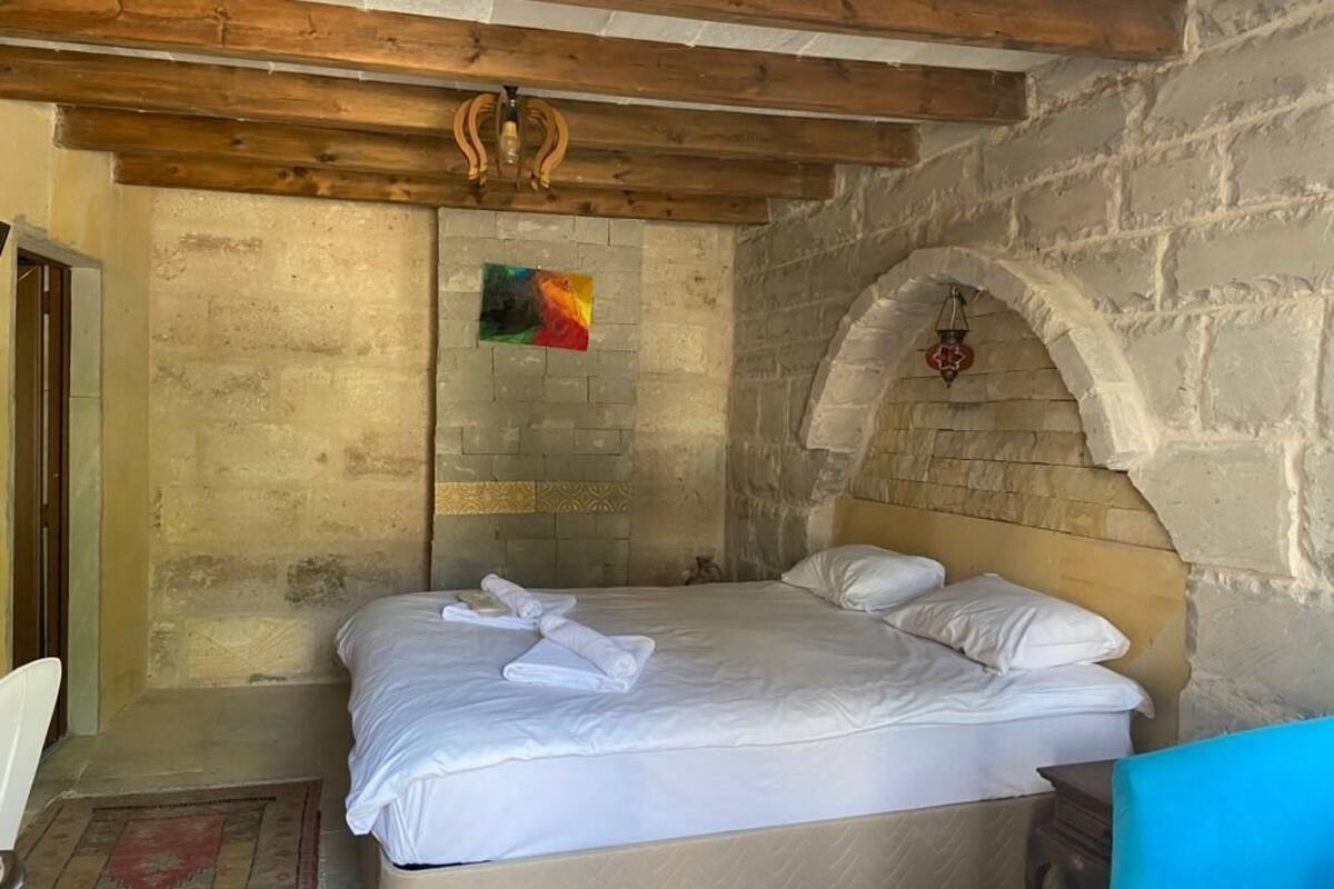 Un dormitorio con cama, techo de madera, pared de piedra y una pequeña ventana en arco.