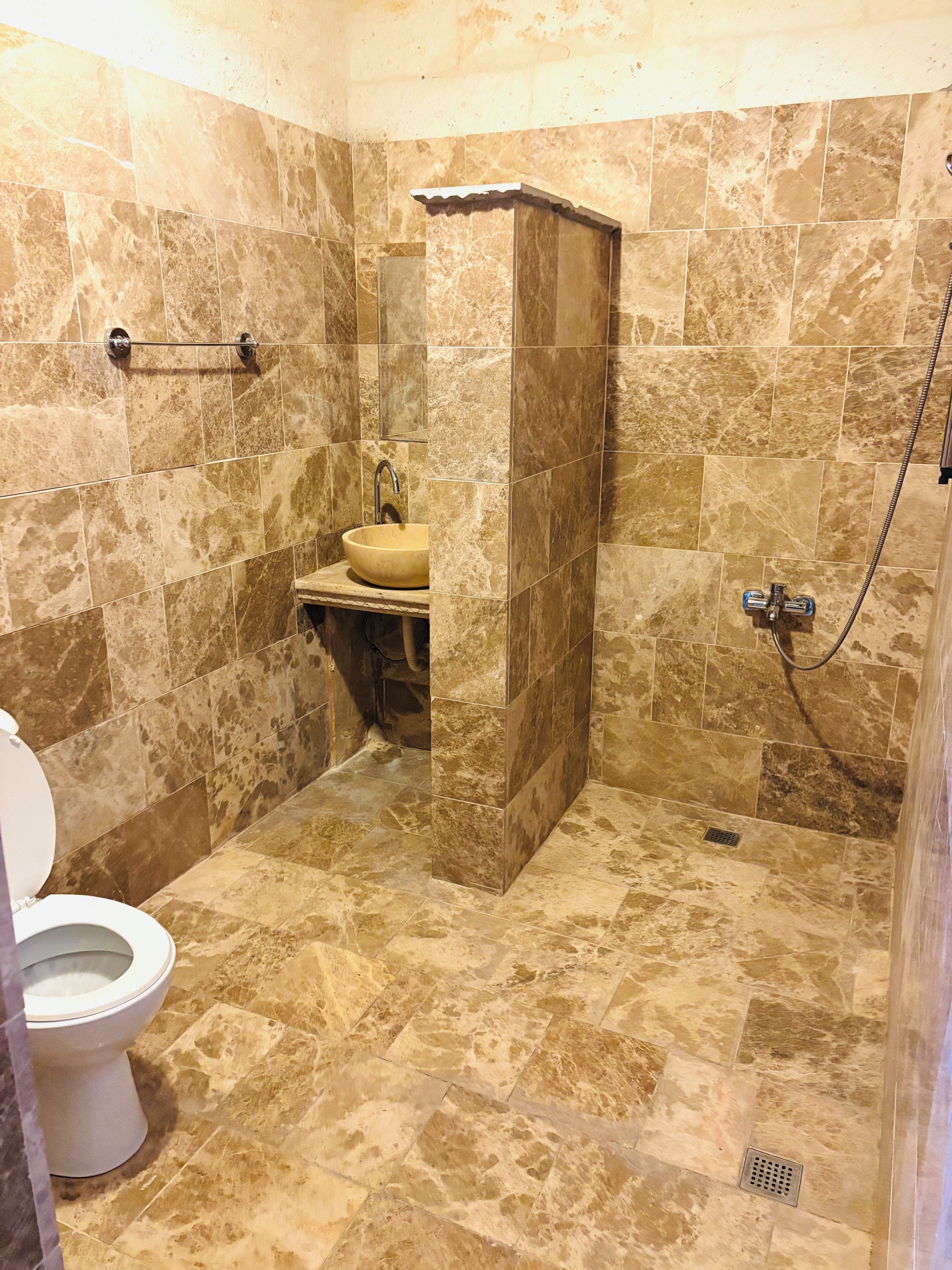 Un baño con inodoro, lavamanos y zona de ducha, con azulejos tipo mármol y ducha a pie.