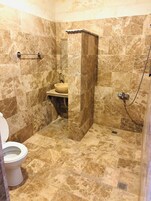 Un baño con inodoro, lavamanos y zona de ducha, con azulejos tipo mármol y ducha a pie.