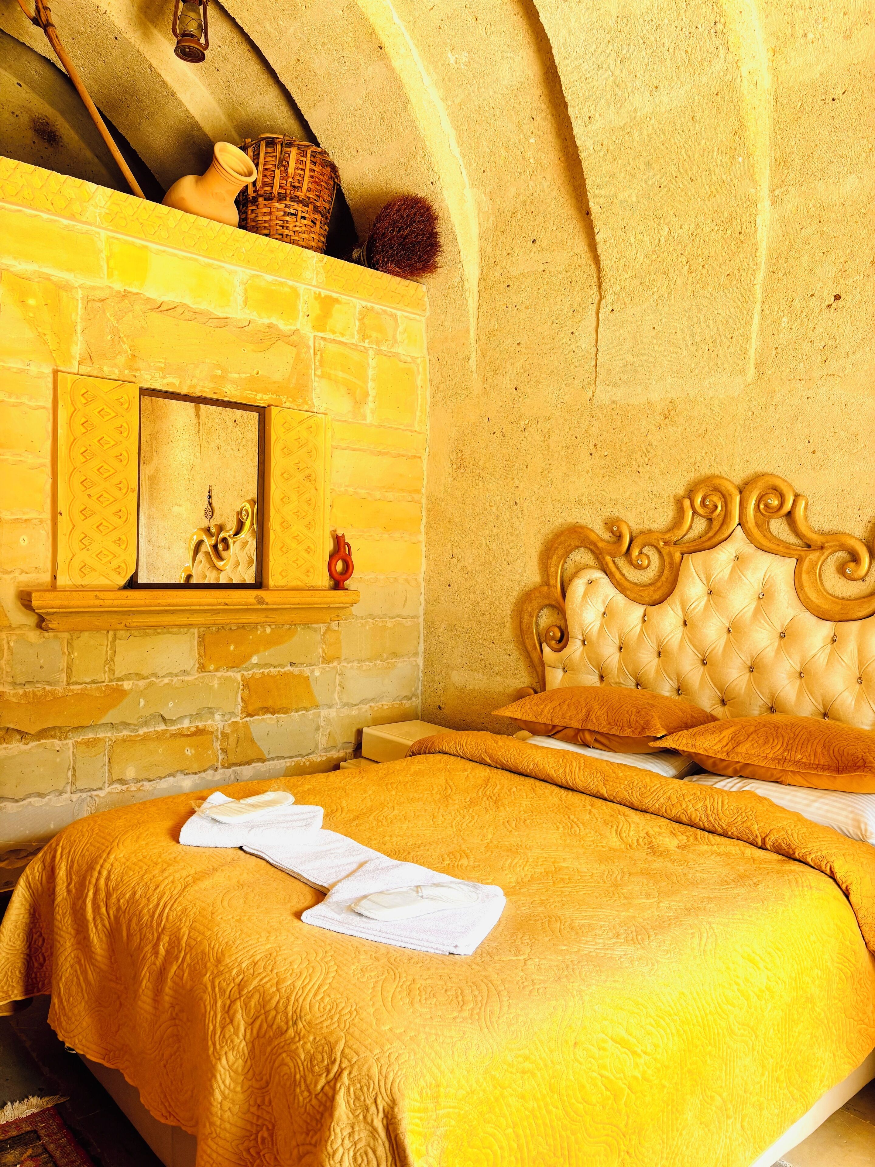 A room with a bed, a wooden headboard, a stone wall, and a fireplace.