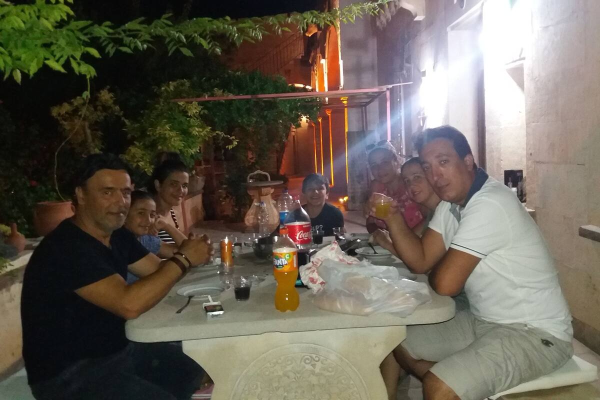 Un grupo de personas sentadas alrededor de una mesa al aire libre por la noche, con una vela, botellas y una bolsa de plástico encima.