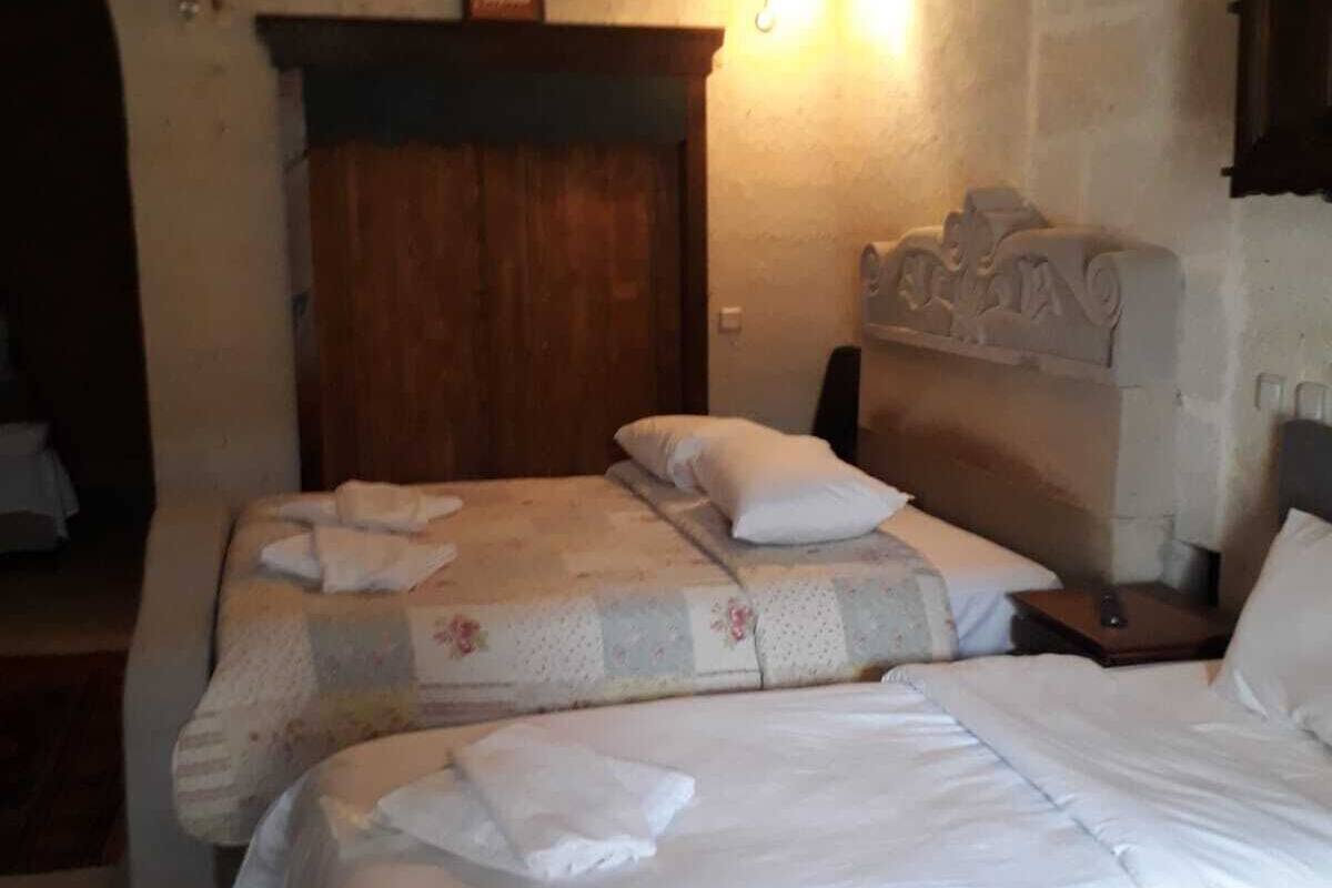 Un dormitorio con dos camas, cabecero de madera, pared de piedra y mesita de noche con lámpara.