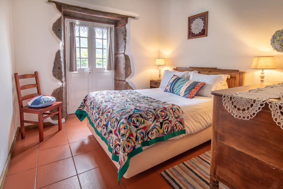 Ein Schlafzimmer mit einem Bett, zwei Nachttischlampen, einem Sessel, einem Holznachttisch und einer Steinwand.