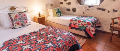 A bedroom with two beds, a stone wall, a window, and a wooden chair.