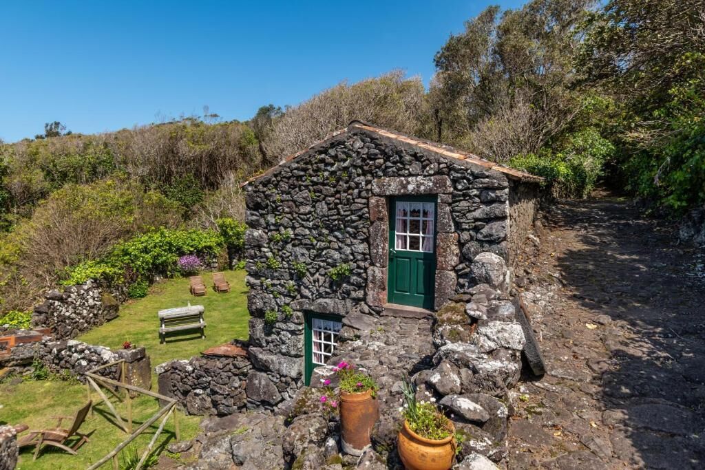 A stone cottage with a green door, a small window, and a bench in the yard.