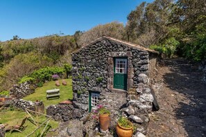 Une petite maison en pierre avec une porte verte, une petite fenêtre et un banc dans la cour.