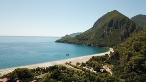 A coastal landscape with a beach, a boat, and a mountainous backdrop.