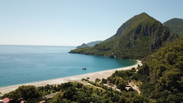 Paisaje costero con playa, un barco y montañas al fondo.