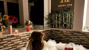 A person relaxing in a hot tub with a glass of red wine, surrounded by plants and flowers.