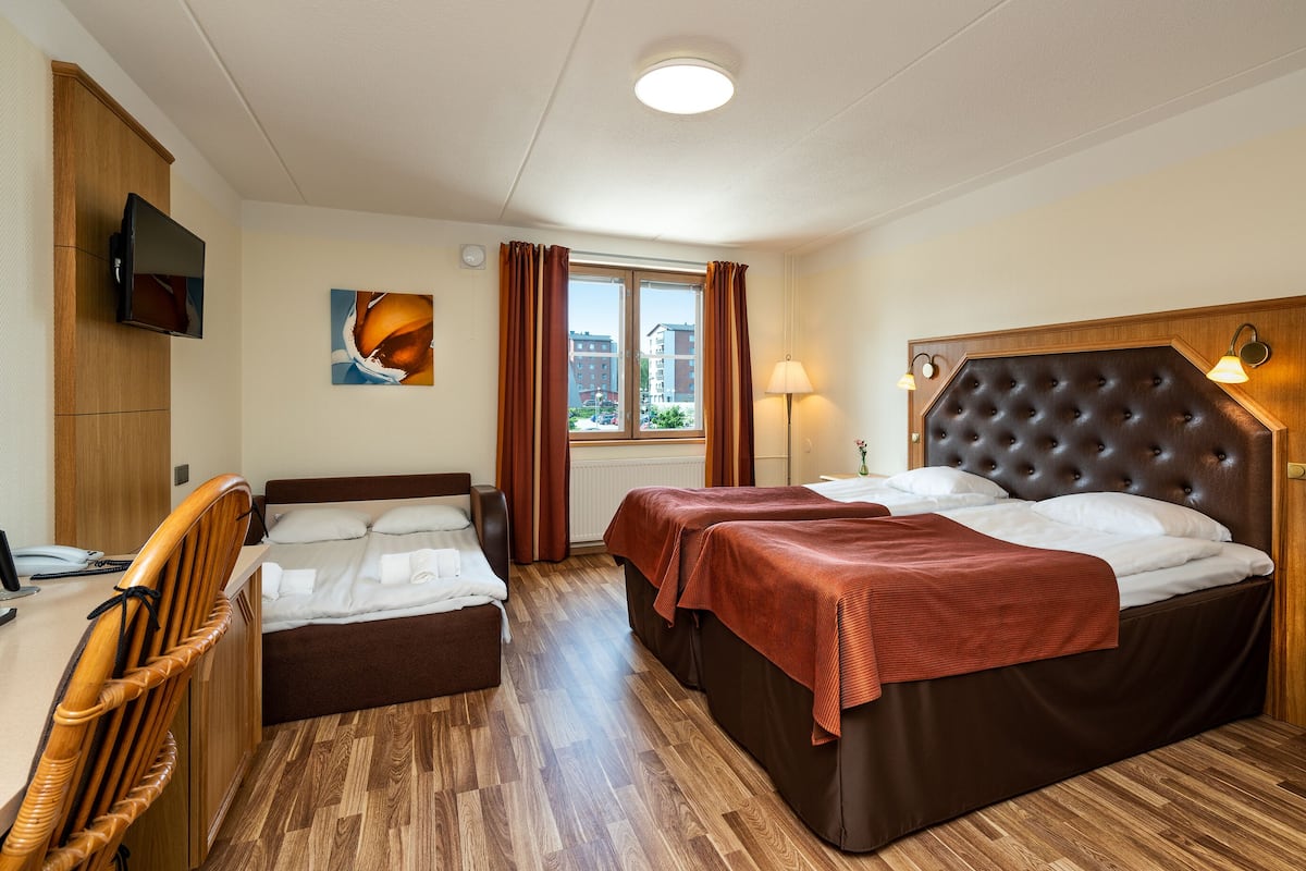 A hotel room with two beds, a desk, a television, a window with curtains, and a lamp.