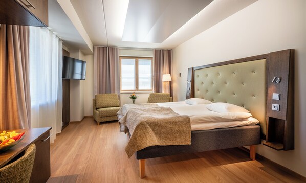 Habitación de hotel con cama, una silla, televisor, ventana con cortinas y una lámpara.