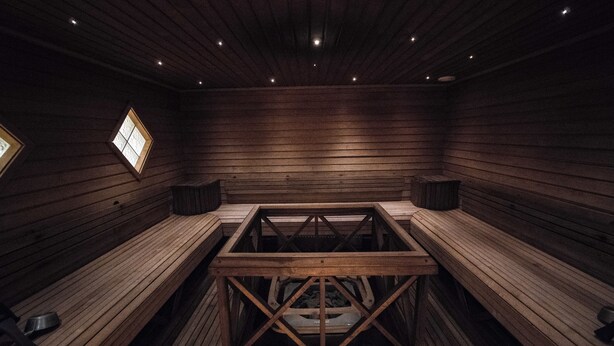 Una sala de sauna con bancos de madera, una estructura central de madera y un ventanal pequeño.