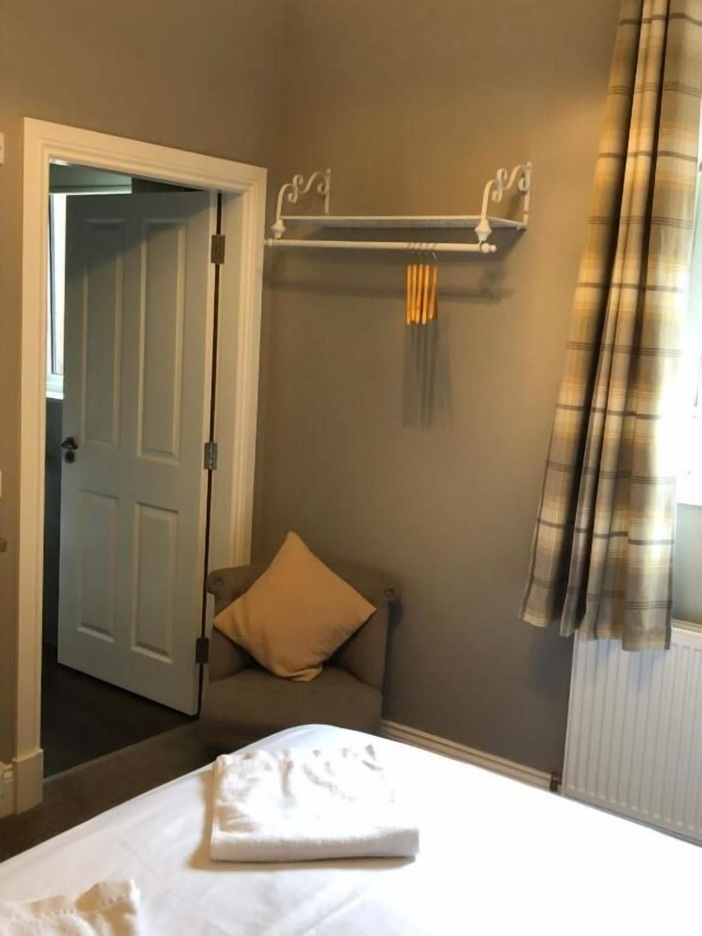 A hotel room with a bed, a chair, a coat rack, and a door leading to another room.
