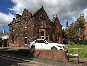 Une maison à deux étages, construite en briques, avec une voiture blanche garée dans l’allée.