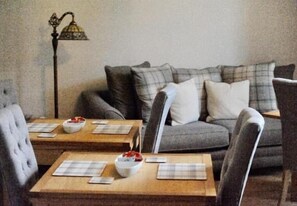 A living room with a sofa, two wooden side tables, and a floor lamp. - The Huntingdon B&B (Dumfries)