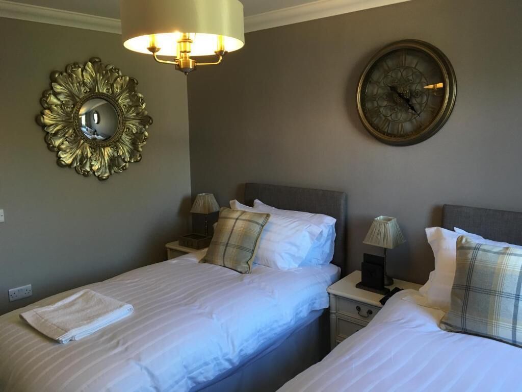 Habitación de hotel con dos camas, un reloj de pared redondo, un espejo decorativo y una lámpara de pared.